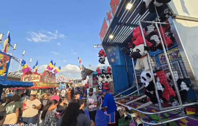 Crowded midway at the Florida Strawberry Festival with carnival games, giant stuffed prizes, and food stands.