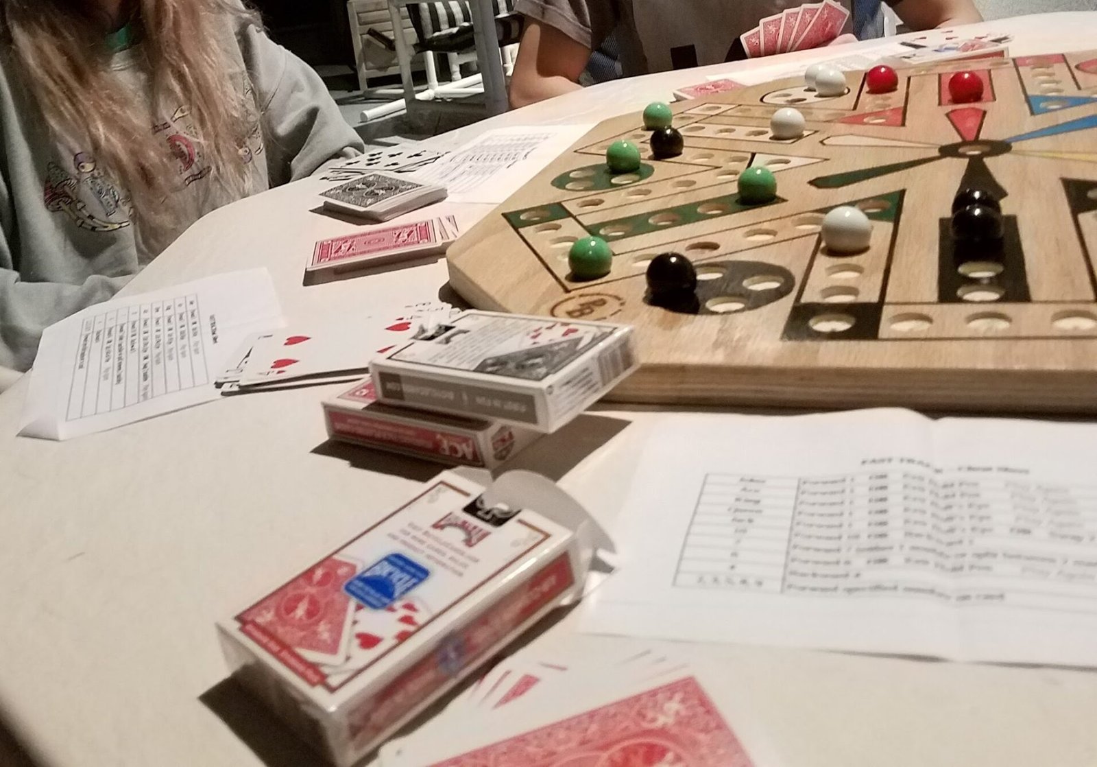 Fast Track marble board game being played with cards, showing colorful marbles on wooden board with card decks and rule sheets on table