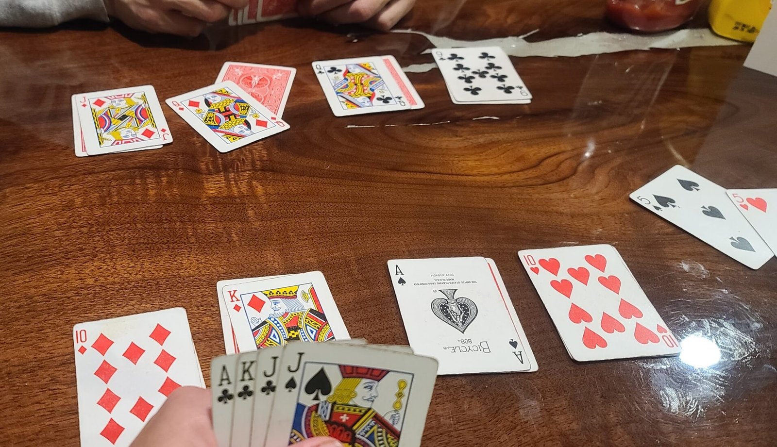 Playing cards spread on a wooden table during a card game with a hand holding Ace, King, and Jacks