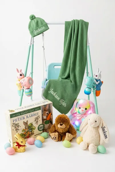 Baby camping Easter basket featuring a portable baby swing surrounded by Easter bunny bubble guns, plush Bigfoot stuffed animal, Deluxe Peter Rabbit gift set, glow-in-the-dark LED bunny, personalized Jackson stuffed bunny, personalized Jackson Tyler baby blanket and hat, gold foil chocolate Easter bunny, and pastel Easter eggs