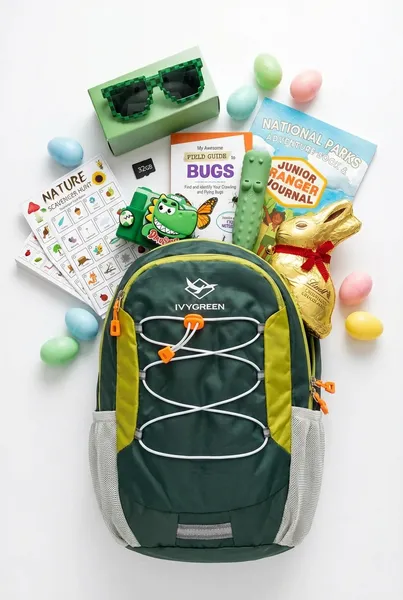 Kids hiking Easter basket made from a green IvyGreen hiking backpack filled with pixel-style kids sunglasses, green dinosaur kids camera, Nature Scavenger Hunt cards, My Awesome Field Guide to Bugs, crocodile kids flashlight, National Parks Junior Ranger Journal, gold foil chocolate Easter bunny, and pastel Easter eggs