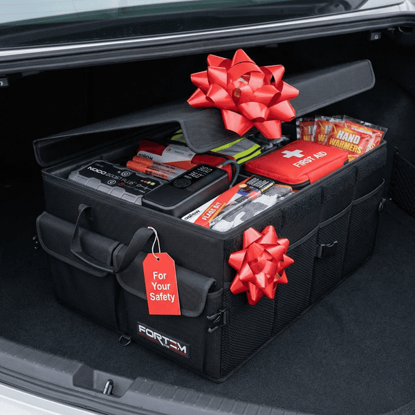 Car trunk organizer filled with emergency kit essentials including a jump box tire inflator road flares and first aid kit with a gift bow making a practical gift for a new driver