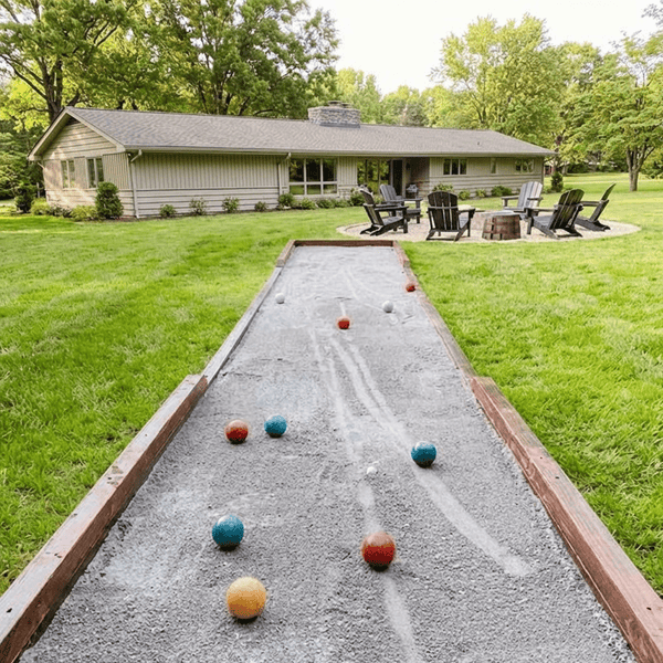 DIY backyard bocce court with crushed oyster shell surface and wooden borders on a sunny lawn