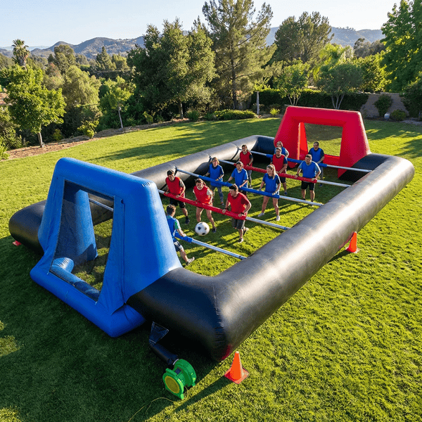 Giant human foosball inflatable arena with two teams holding poles competing on a sunny lawn