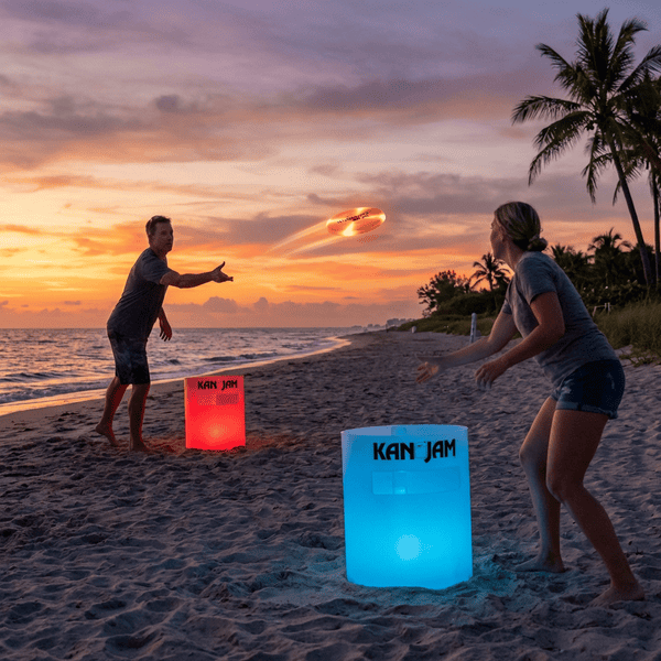 Kan Jam disc toss game glowing on a beach at sunset with two adults throwing a frisbee