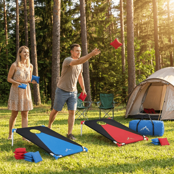 Portable collapsible cornhole set with blue and red boards and bean bags on a sunny campsite lawn