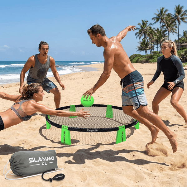 Four adults playing Slammo roundnet game on a sunny beach laughing and competing