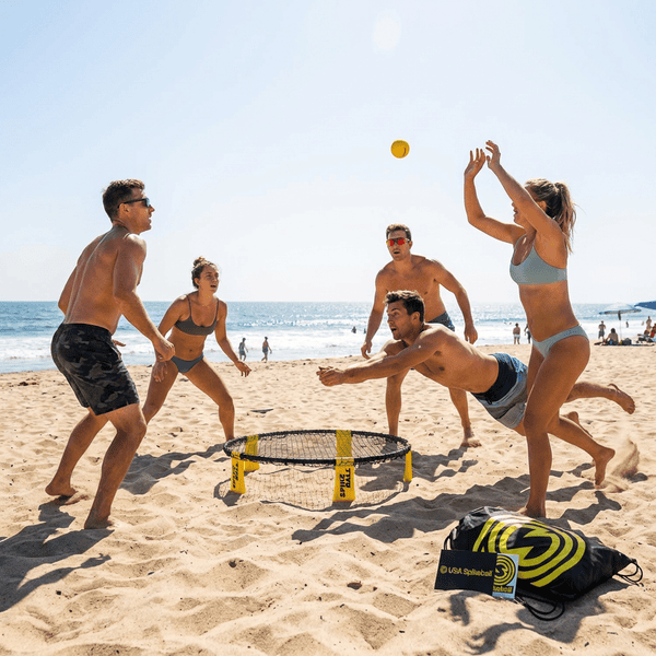 Four adults playing Spikeball on a sunny beach diving and competing around the small round net
