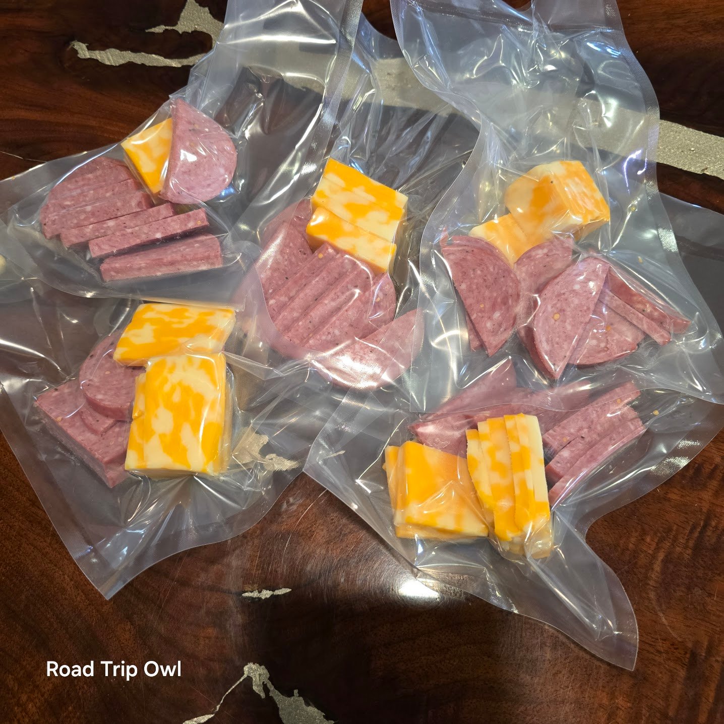 Individual vacuum-sealed snack packs of summer sausage and cheese, prepped at home for road trips and cooler-friendly travel snacking.