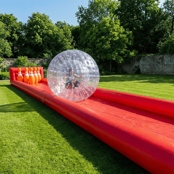 Giant zorb ball human bowling game with oversized inflatable pins set up on a sunny backyard lawn