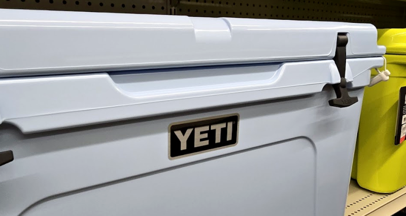 Close-up of YETI rotomolded coolers (pastel blue, neon yellow) on a store shelf, showing the T-latches and YETI logo