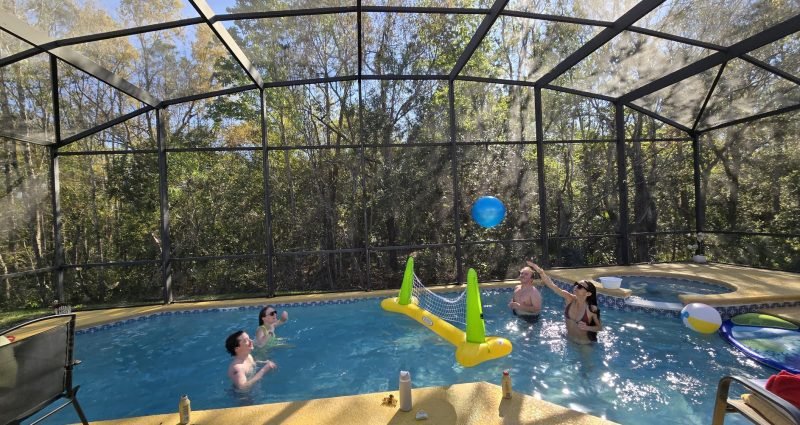A family playing pool volleyball in a screened Florida vacation rental — the kind of easy, unstructured family time that makes a first vacation feel like a success.
