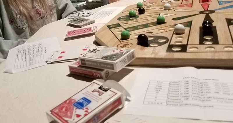 Fast Track marble board game being played with cards, showing colorful marbles on wooden board with card decks and rule sheets on table